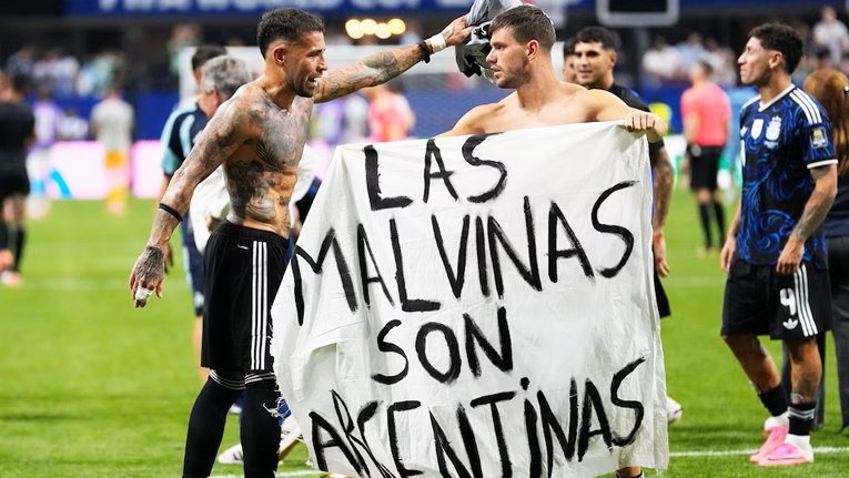Jugadores de la Selección argentina con una bandera que dice Las Malvinas son argentinas en el césped de un estadio