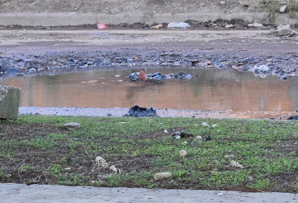 Calle de tierra con agua acumulada y zanjas en el barrio Ampliación Congreso, San Miguel de Tucumán